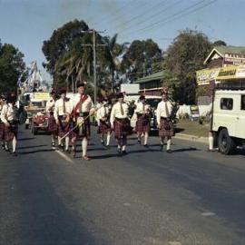 Scottish pipe band passing Pelican Bill's shop, Festival of Waters parade, Noosaville, 25 August 1979