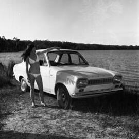 Bikini model posed beside Ford Escort, 1970 