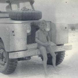 Boy sitting on front of a car on the beach, ca 1970